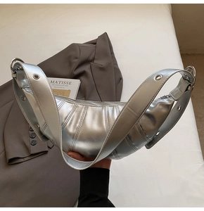 Detail of silver crescent bag with pleated texture and wide strap with metal eyelets