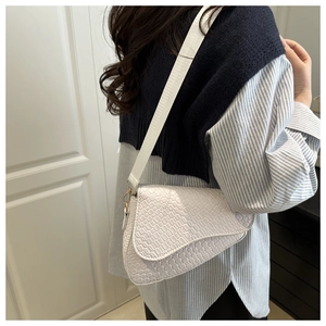 Detailed close-up of white saddle bag with crocodile texture and gold hardware on model