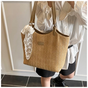 Close-up of woven straw tote bag with brown leather handles and white lace bow detail
