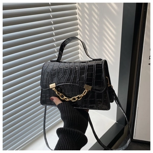 Detail of black crocodile texture bag with gold chain and handle in natural light