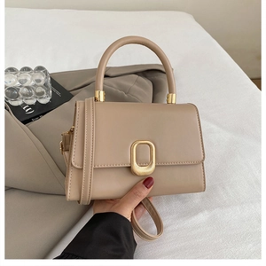 Close-up of cream-colored crossbody bag with elegant gold oval buckle and top handle
