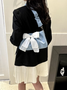 Back view of light blue shoulder bag with large white bow on a black blazer