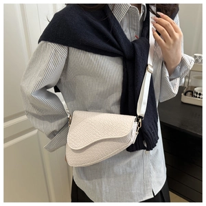 Detailed shot of white crocodile embossed saddle bag with wide adjustable strap on model