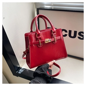 Detail of red leather handbag with gold twist lock and decorative belt strap accents