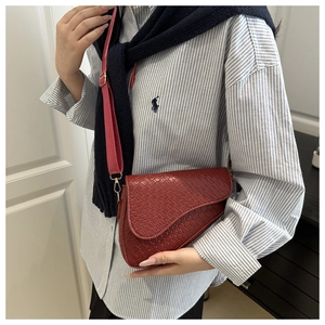 Close-up of wine red saddle bag featuring crocodile texture and wide fabric strap