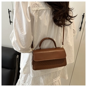 Close-up of brown textured crossbody bag with woven details worn with a white lace dress
