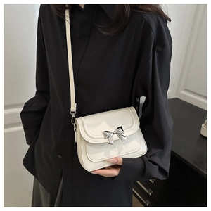 Detail of cream crossbody bag with silver bow accent and adjustable shoulder strap