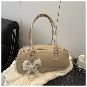 Detail of beige patent leather handbag with lace bow and pearl pendant on white surface