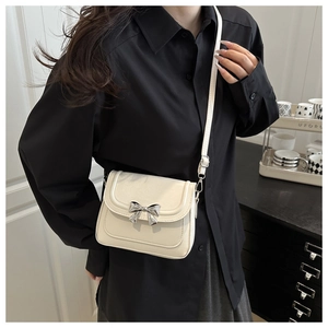 Close-up of a cream-colored crossbody bag with a metallic silver bow on the flap