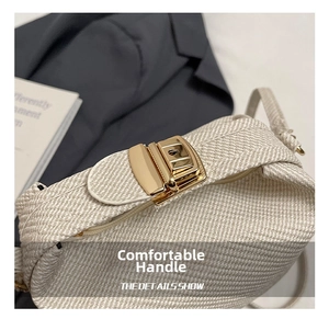 Detail of woven beige shoulder bag showing golden rectangular metal buckle and fabric texture