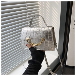 Detail of silver crocodile-embossed handbag featuring a chunky gold metal chain link decoration