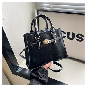Detail of black crackle leather handbag featuring a gold twist lock and sturdy handles