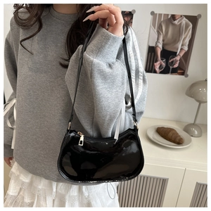 Sac sous le bras en cuir verni noir avec zip doré porté par un mannequin
