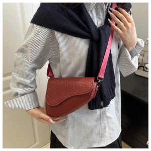 Detail of woven burgundy saddle bag featuring gold metal buckles and pink braided strap