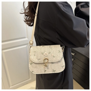 Detail showing woven texture and floral embroidery on a white crossbody straw bag