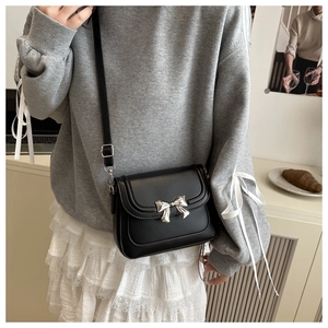 Detail of a black leather crossbody bag with silver bow buckle on model in studio
