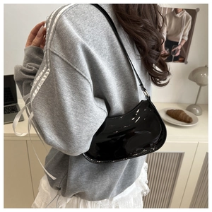 Detail of glossy black patent leather crescent shoulder bag worn on a model's arm