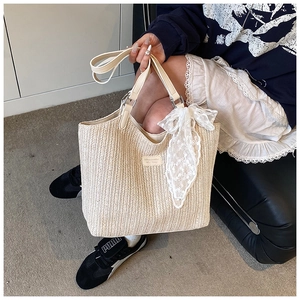 Detail of woven straw tote bag featuring white lace bow and leather handle straps