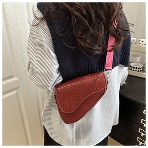 Close-up of wine red saddle bag with crocodile texture and pink woven shoulder strap
