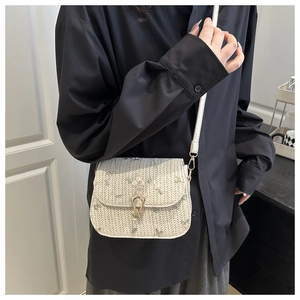 Detail view of floral embroidery and gold horseshoe buckle on woven straw crossbody bag