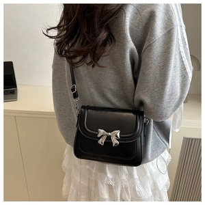 Detail of black leather square bag with silver metal bow and adjustable shoulder strap