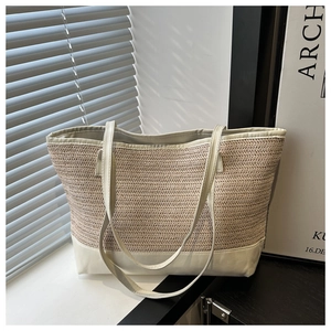 Detail of a beige woven straw tote bag with white leather straps and herringbone texture