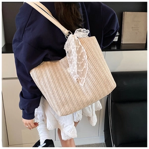 Detailed view of beige woven tote bag featuring a delicate white lace scarf decoration