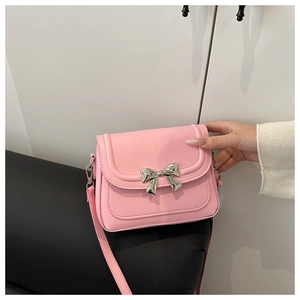 Close-up of pink leather crossbody bag featuring a silver metal bow accent and strap