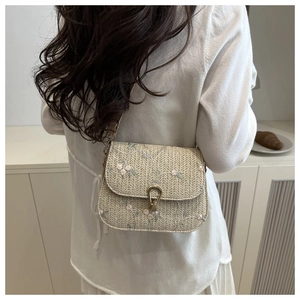 Detail of a straw saddle bag featuring pink floral embroidery and golden clasp