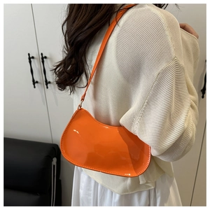 Vue détaillée d'un sac baguette en cuir verni orange vif porté à l'épaule