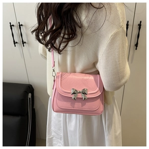 Detailed view of pink crossbody bag with silver bow ornament on a soft beige sweater