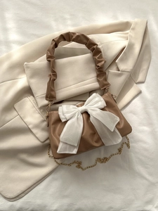 Detail of a brown leather bag with a white organza bow and ruched handle on a blazer