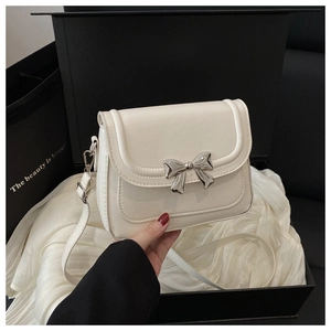 Detail of creamy white crossbody bag with silver bow ornament on premium matte leather