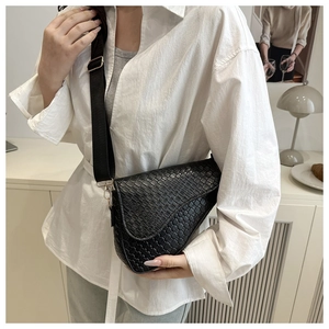 Detail of black saddle bag with woven texture, wide strap and golden metallic hardware
