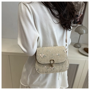 Detailed close-up of straw crossbody bag featuring floral embroidery and gold metal lock