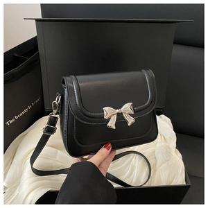 Detail of silver bow metal clasp on black leather crossbody bag inside a luxury gift box