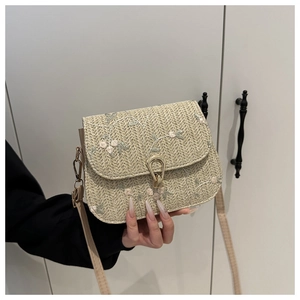 Close-up of floral embroidery and gold metal clasp on beige straw crossbody bag