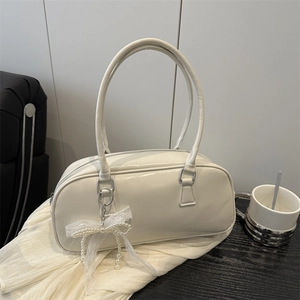 Minimalist white glossy bowling handbag with lace bow charm on soft white fabric background