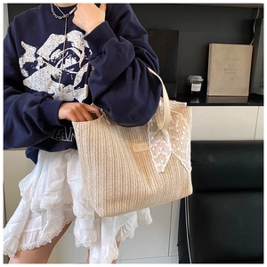 Detail of straw tote bag with lace bow, leather handles and brand logo tag