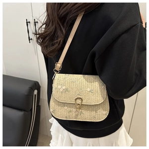 Detail of beige straw saddle bag featuring floral embroidery and gold metal buckle