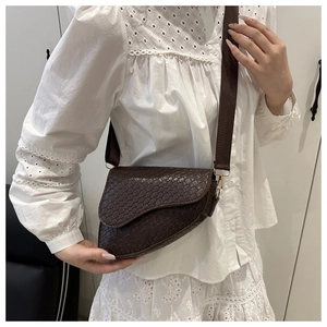 Deep brown saddle bag with woven texture and wide strap worn on a white lace shirt