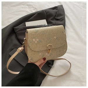 Detail of floral embroidery on a beige straw bag with a gold buckle and leather strap