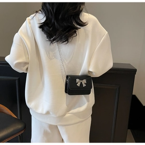 Détail d'un sac bandoulière noir avec nœud argenté et chaîne sur un sweat-shirt blanc
