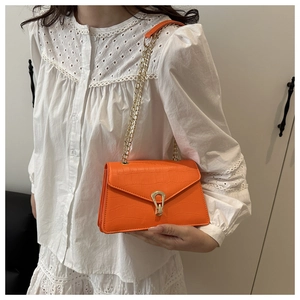 Close-up of bright orange embossed crossbody bag with gold horseshoe clasp and chain