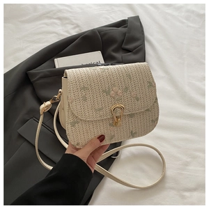 Detail of floral embroidery and gold horseshoe clasp on the cream woven straw bag