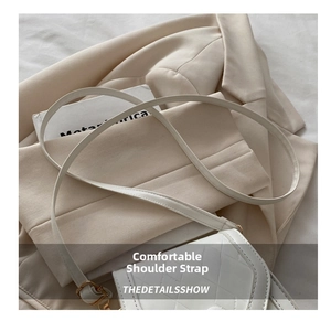 Close-up of white quilted crossbody bag with metal buckle on beige blazer background