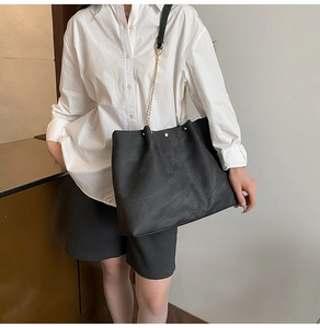 Detail of black faux leather tote with golden chain strap and textured matte finish