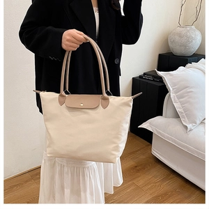 Détail d'un cabas en nylon beige avec anses en cuir marron porté sur un blazer noir chic