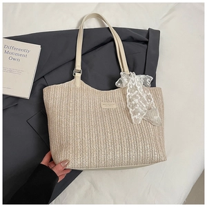 Detail of woven straw tote bag featuring cream leather handles and white lace bow detail