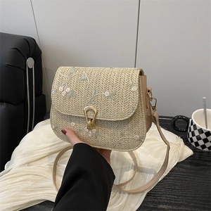Straw saddle bag with floral embroidery and gold buckle shown in a lifestyle setting